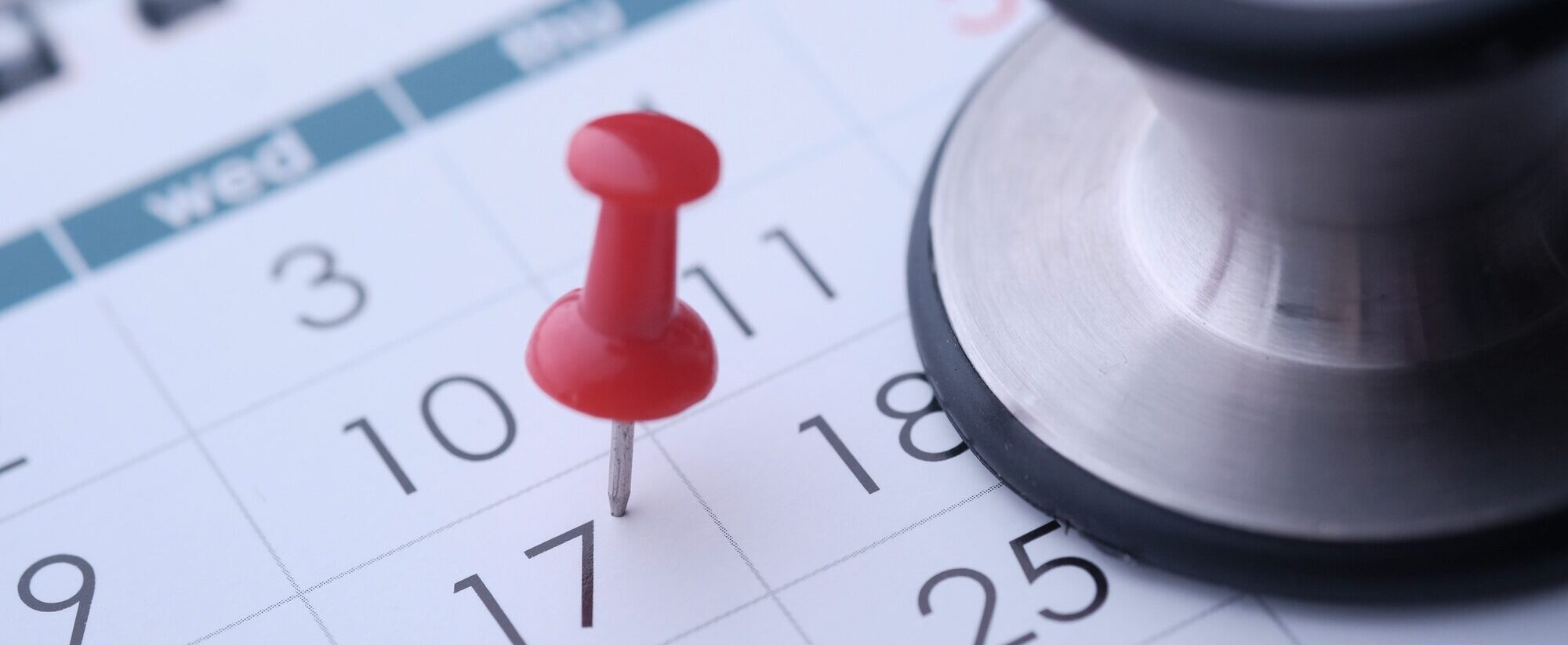 A stethoscope and a red thumbtack placed on a calendar signify health appointments and schedules